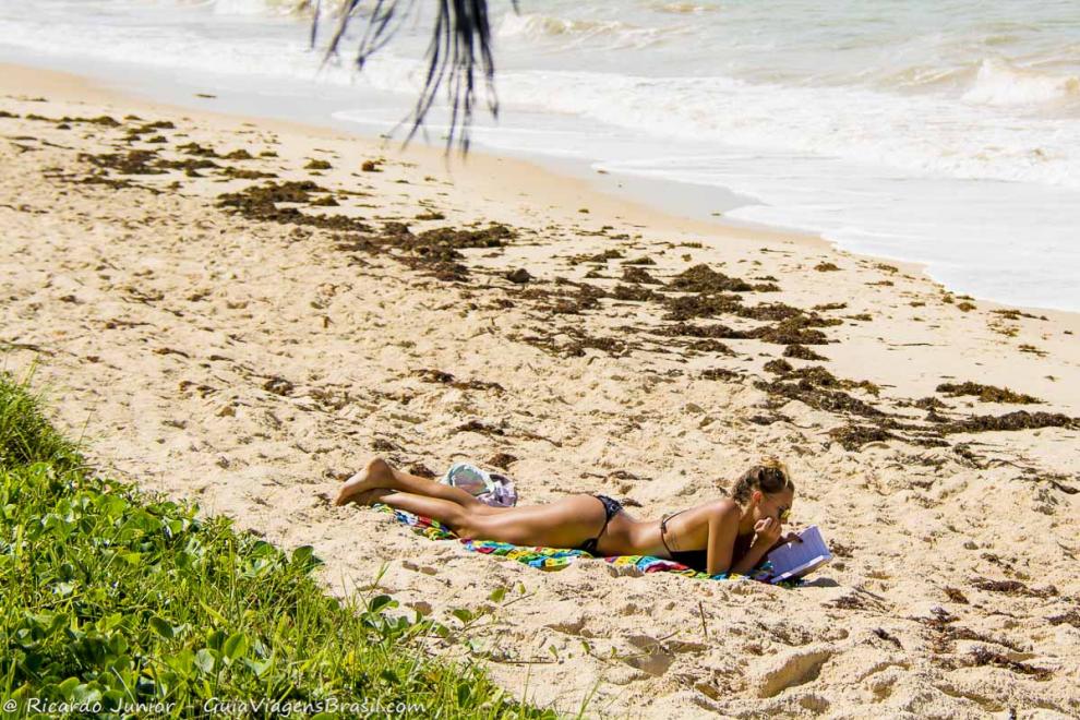 Imagem de uma moça lendo e tomando sol nas areias lindas da Praia de Araçaípe.